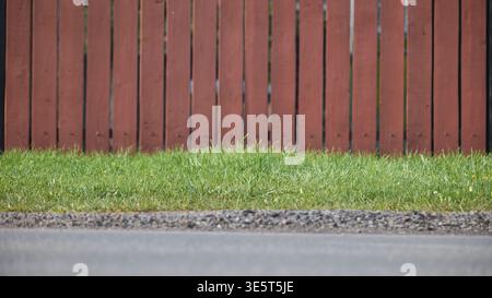 Brown wooden fence separating green grass lawn from road and gravel path Stock Photo
