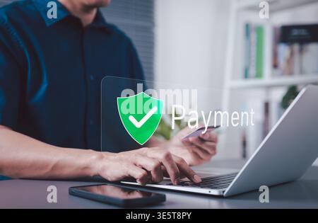 Secure Payment and Trusted Transaction Concept. A man using a laptop and smartphone with payment shield icon representing secure checkout, digital Stock Photo