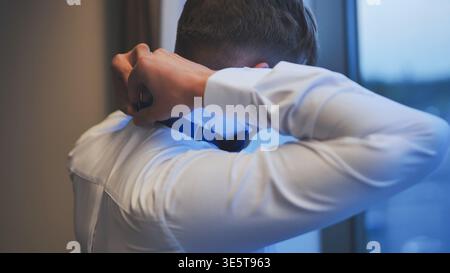 Man in a white shirt adjusts a blue bow tie, seen from behind. Stock Photo