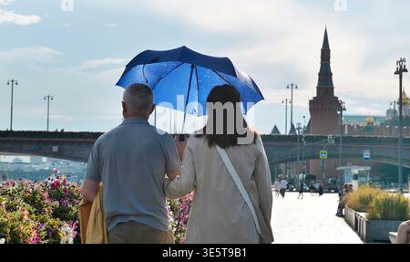 Senior couple walking with umbrella on Moscow embankment, enjoying sunny day Stock Photo
