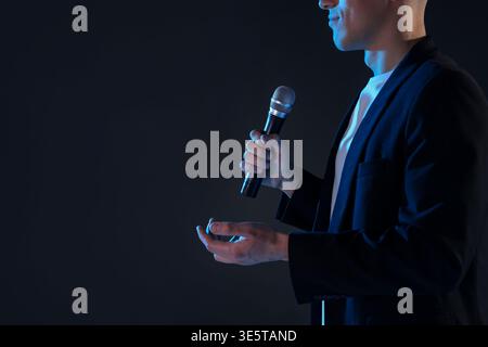 Presenter with microphone performing on dark background, closeup. Space for text Stock Photo
