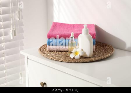 Stack of colorful towels, cosmetic products and plumeria flower on white dresser indoors Stock Photo