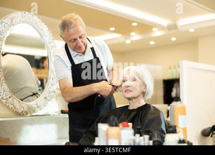 Experienced hairdresser using curling wands to add volume to older lady Stock Photo