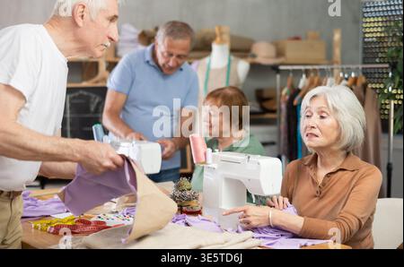 Some people communicate and discuss pattern, while others sew using sewing machine at lesson Stock Photo
