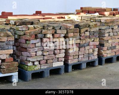 Stack of reclaimed old bricks on wooden pallets. Vintage rustic clay bricks for construction, renovation, and landscaping. Pile of salvaged masonry Stock Photo