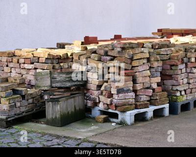 Stack of reclaimed old bricks on wooden pallets. Vintage rustic clay bricks for construction, renovation, and landscaping. Pile of salvaged masonry Stock Photo