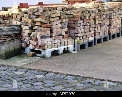 Stack of reclaimed old bricks on wooden pallets. Vintage rustic clay bricks for construction, renovation, and landscaping. Pile of salvaged masonry Stock Photo