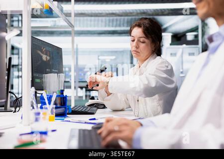 Researcher using computer application for DNA data analysis in laboratory waiting for results. Research facility specialist checking time on wrist watch, using bioinformatics genomics software Stock Photo