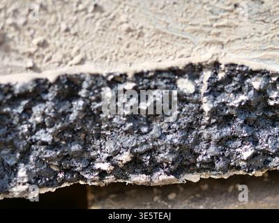 Extreme close-up asphalt and concrete edge, cross-section of road construction materials,  gritty black bitumen texture, rough grey cement surface, in Stock Photo