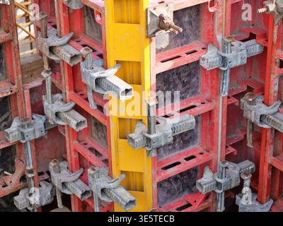 Industrial concrete formwork system, red and yellow steel shuttering panels, close-up of heavy duty metal clamps and scaffolding connectors, professio Stock Photo
