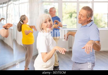 Cheerful senior lady practicing twist with male partner in dance studio Stock Photo