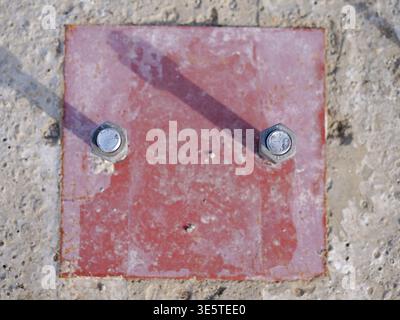 Top-down view heavy duty anchor bolts in red steel base plate, industrial construction fasteners  set in concrete, architectural mounting hardware det Stock Photo