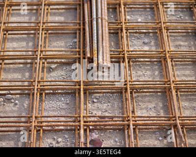 Close-up side view of industrial anchor bolts set in a red steel base plate, heavy-duty threaded  studs with silver hex nuts on a weathered concrete f Stock Photo