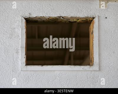 close up photo of empty rectangular window opening in white plastered wall, renovation site  with missing window frame, dark interior visible through Stock Photo
