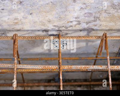 rusty steel rebar cage for concrete reinforcement, metal mesh structure for  building foundation with plastic star spacers, grey concrete wall in bac Stock Photo