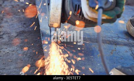 Worker using an angle grinder, cutting metal with sparks flying at construction site Stock Photo