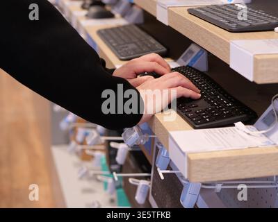 Person typing on a black wireless keyboard. Hands on keyboard in a computer store. Close up of electronic device display on wooden shelf. Shopping for Stock Photo
