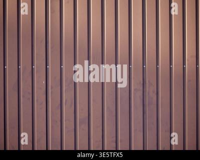 , full-frame shot of a brown corrugated metal fence with vertical ridges and visible silver screw heads. The surface shows a slightly weathered, matte Stock Photo