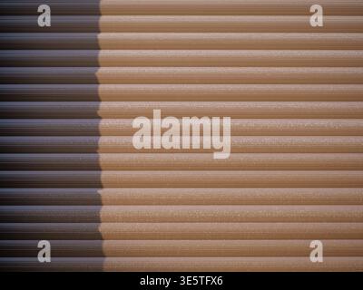 brown texture roller shutter or garage door with horizontal grooved slats. The surface shows a fine, speckled texture with subtle reflections of light Stock Photo