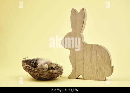 Wooden rabbit and nest with small eggs on yellow background, Happy Easter card Stock Photo