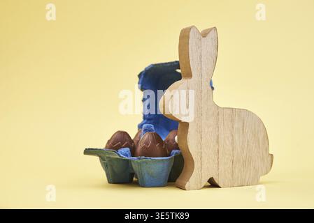 Wooden rabbit and chocolate eggs on yellow background, Happy Easter card Stock Photo