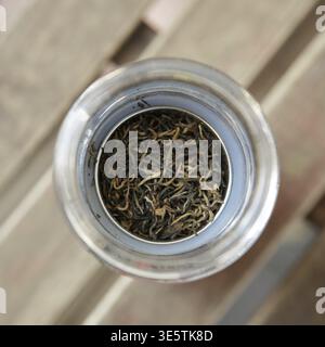 This closeup shows dried tea leaves in a glass jar, elegantly placed on a rustic wooden background Stock Photo