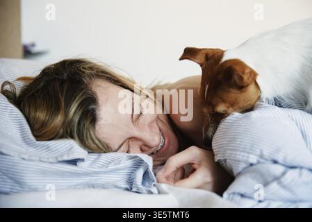 Woman lying in bed and playing with her dog, Lazy weekend, Morning relax Stock Photo