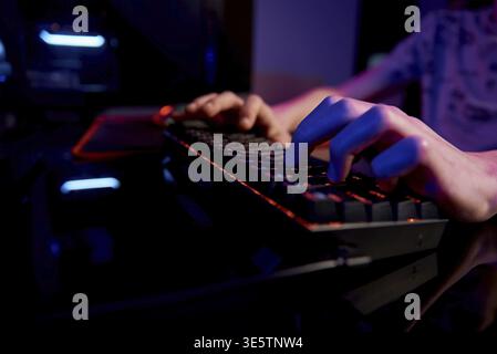 Professional gamer play computer video game in dark room, use neon colored rgb mechanical keyboard, place for cybersport gaming Stock Photo