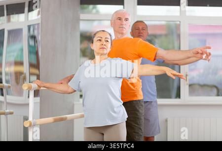 Close-up view of mature woman practicing ballet positions standing by ballet-barre Stock Photo