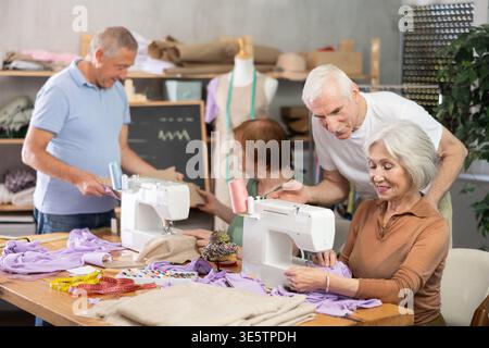 Some people communicate and discuss pattern, while others sew using sewing machine at lesson Stock Photo