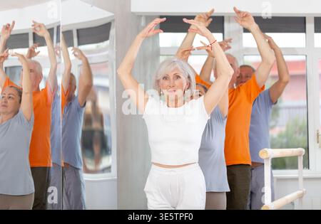 Active mature woman practicing fifth position holding by ballet barre together with others Stock Photo