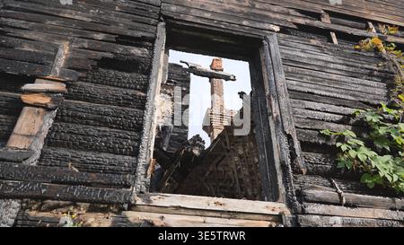 Burnt wooden house wall with an empty window frame and a distant brick chimney Stock Photo