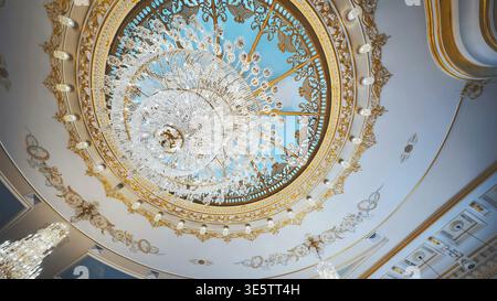 Low angle view of a grand crystal chandelier in a luxury hall. Ornate gold dome with painted blue sky. Stock Photo
