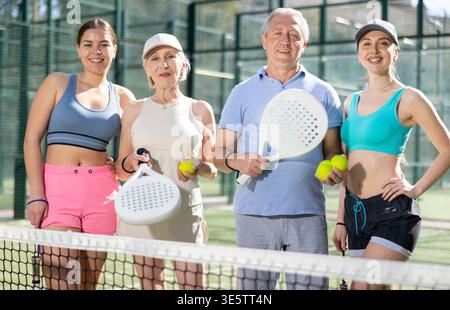 A group of tennis players posing next to the net holding Padel rackets Stock Photo