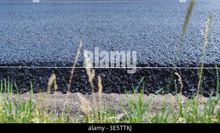 Fresh asphalt road surface with new layers during construction along grassy roadside Stock Photo