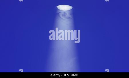 Bright stage spotlight illuminating an area with hazy smoke against a deep blue background Stock Photo