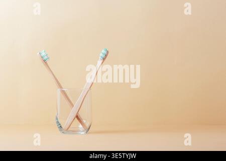 Bamboo toothbrushes in glass cup on beige pastel background, eco friendly dental care and hygiene concept. Front view, copy space. Stock Photo