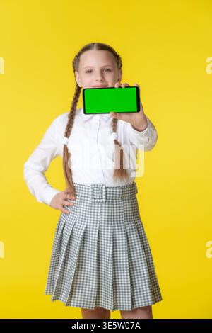 Confident student in school uniform with braids holds smartphone with green screen. Ideal for educational app advertising and technology mockups. Brig Stock Photo