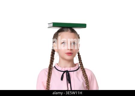 Portrait of surprised girl with pigtails balancing book on head to improve posture. Concept of learning, concentration and education. Studio shot isol Stock Photo