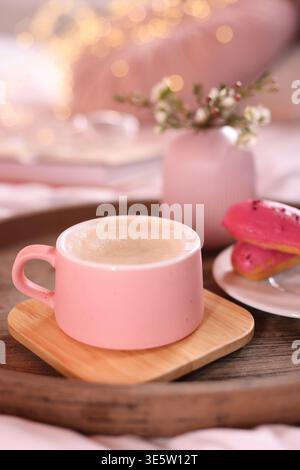 Aromatic coffee in cup, eclairs, and beautiful flowers on bed, closeup Stock Photo