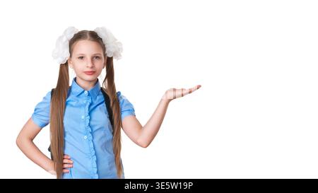 Confident schoolgirl in blue uniform with pigtails gestures with an open palm, presenting copy space. Student with backpack isolated on white backgrou Stock Photo