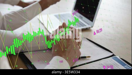 Showing man in white shirt clasping hands on notebook at table with laptop, pen, market charts Stock Photo