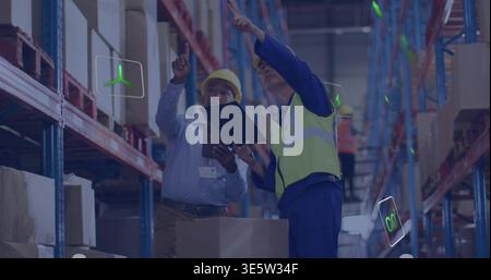 Checking warehouse stock, workers in yellow helmets with clipboard pointing at pallet and AR icons Stock Photo