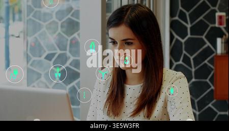 Working woman typing on open laptop at cafe, wearing white polka-dot blouse with green overlays Stock Photo