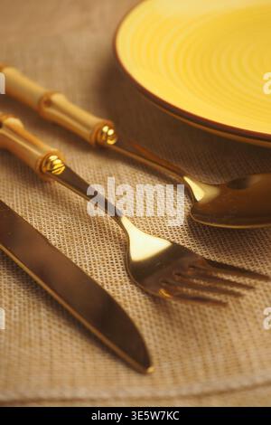 Set of gold cutlery on a table with a yellow plate Stock Photo