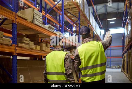 Back view of warehouse workers checking racks and planning inventory logistics Stock Photo