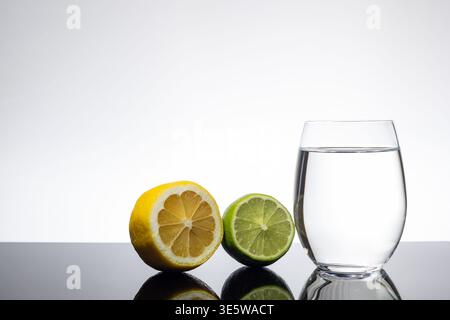 Sliced Lemon and Lime Beside Glass of Clear Water on White Background with Copy Space Stock Photo