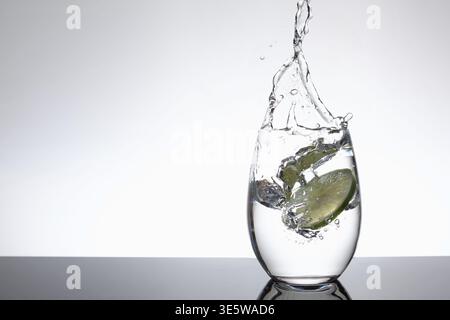 Lime Slice Splashing into Glass of Water with Dynamic Splash on White Background and Copy Space Stock Photo