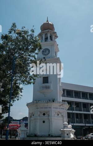 White clock tower stands tall against clear sky. Decorative arches frame its ornate clock face. Tree branches frame the tower's left side. Modern buil Stock Photo