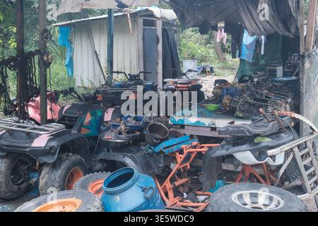 Abandoned shed with broken machinery and scattered tools. Worn tires lie beside broken equipment and debris. Blue bucket sits among scattered metal fr Stock Photo